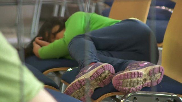 A young asylum seeker sleeping on wooden chairs.