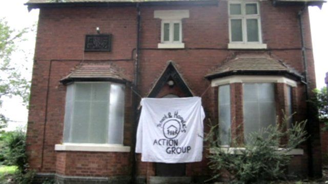 A house with boarded windows and a homeless action group flag outside