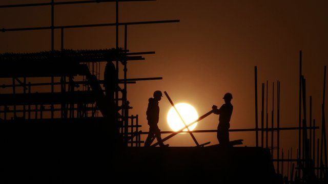Construction workers install scaffolding on a building at sunset in Shanghai