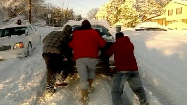 Three people pushing a car stuck in the snow