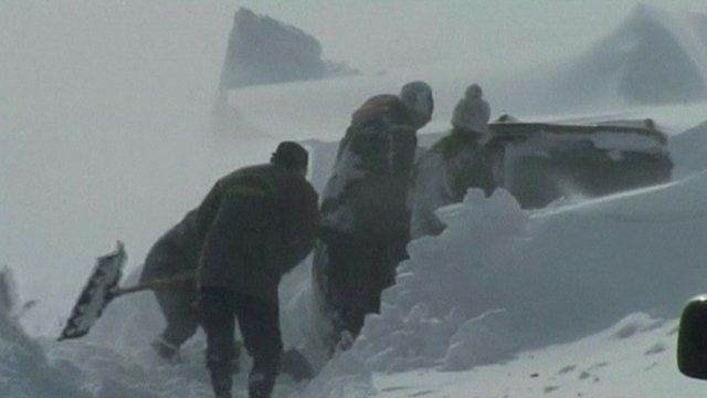 Workers dig out a car buried in snow