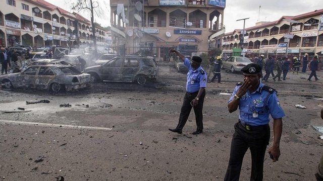 Policemen walk towards burnt vehicles at the scene of a blast at a business district in Abuja