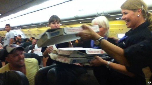 A Frontier Airlines flight attendant passes out pizza to passengers