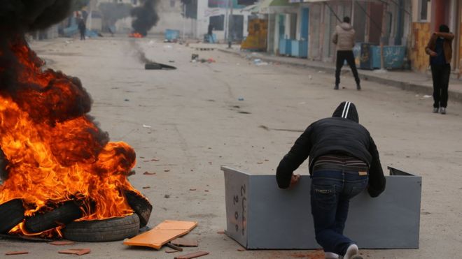 எல்லை கடந்து வர்த்தகம் மேற்கொள்வதற்கு தடைவிதித்திருப்பதால் கோபம் அடைந்துள்ள பகுதியான லிபியாவின் எல்லைக்கு அருகிலுள்ள ஒரு நகரின் காவல் நிலையத்தின் மீது கற்களை எறிகின்ற துனிஷிய இளைஞர்கள்.