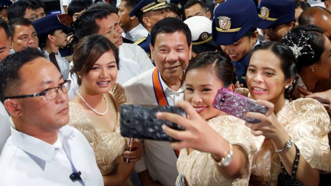 Philippines President Rodrigo Duterte is having his pictures taken with three girls as they attend a ceremony