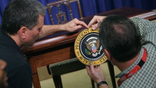 Workers affix the US presidential seal on a desk in the White House