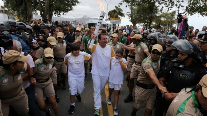Mayor Eduardo Paes (C) carries the Olympic torch just after it was transported across Guanabara Bay from Niteroi to Rio de Janeiro three days before the official start of the Rio 2016 Olympic Games,