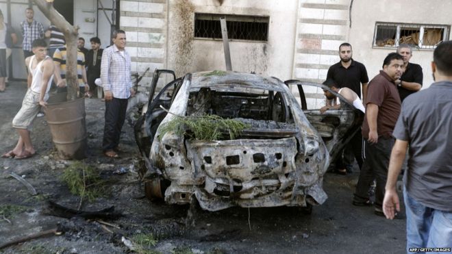 Palestinians gather around a burnt-out car in Gaza City on July 19, 2015, after explosions destroyed five cars in Gaza