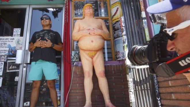 A man poses next to a Donald Trump statue in Los Angeles