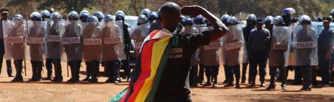 A demonstrator wrapped in a Zimbabwean flag salutes riot police in Harare - August 2016