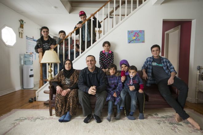 The inside Al Jasem family pose for a picture starting left to right on the couch, Mother Sawsan and father Abdel Malek, their kids, Walaa, Alaa, Khitam, Fadl, and Ramaz, and standing on the staircase left to right, Sleiman Abdel Malek, Madjid, Bachar, and Ahmad, inside their temporary home in Picton, Ontario, Canada,