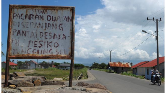 A motorist rides past a board that, in the local language, reads "If you date on the beach, the risk is on your own" in Banda Aceh