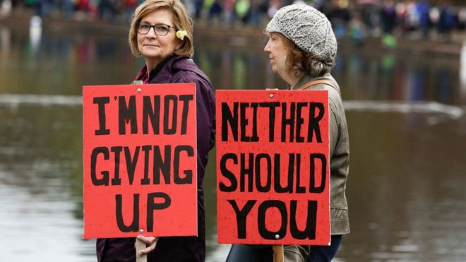 Dos mujeres en Seattle sostienen carteles de protesta en una de las residencias de Trump