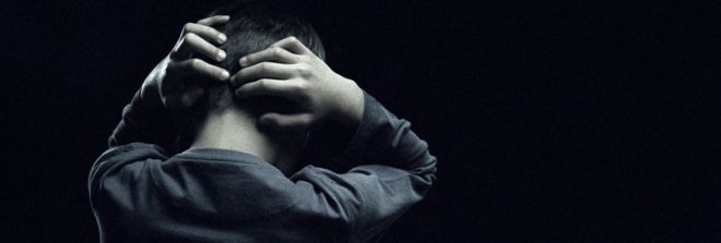 A boy or young man with his hands on his heads. His back is to the camera and his face is not visible