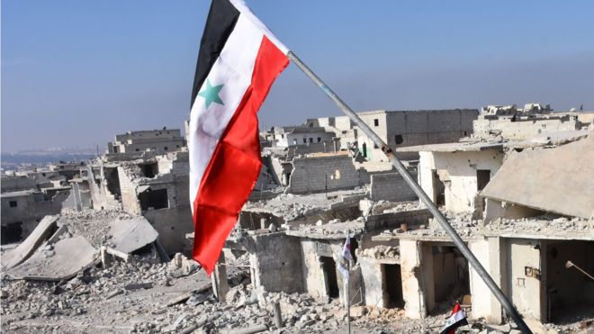 Syrian flag flies over destroyed buildings in Aleppo's Sheikh Saeed district, on December 12, 2016, after Syrian pro-government forces retook the area from rebel fighters.