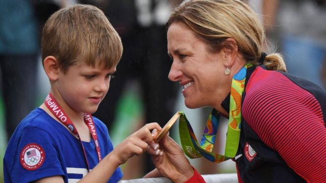 La ciclista estadounidense Kristin Armstrong le muestra su medalla de oro a su hijo.