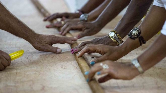 Workers help Cuban cigar roller Jose "Cueto" Castelar, hand roll a 90-meter cigar, in Havana, Cuba, Friday, Aug. 12, 2016.