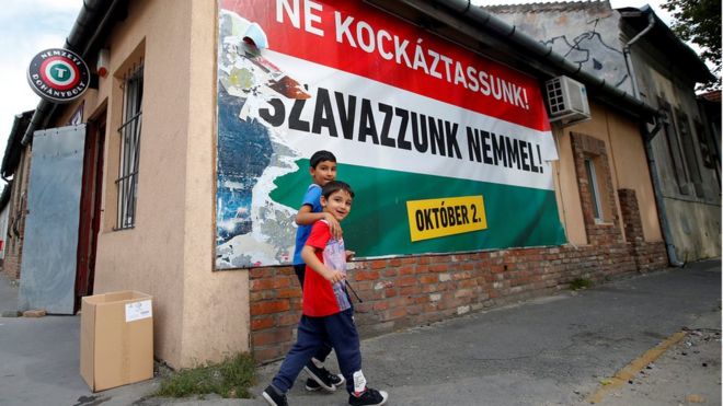 Hungarian Roma boys walk in front of the Hungarian government's poster regarding referendum on EU migrant quotas in Budapest