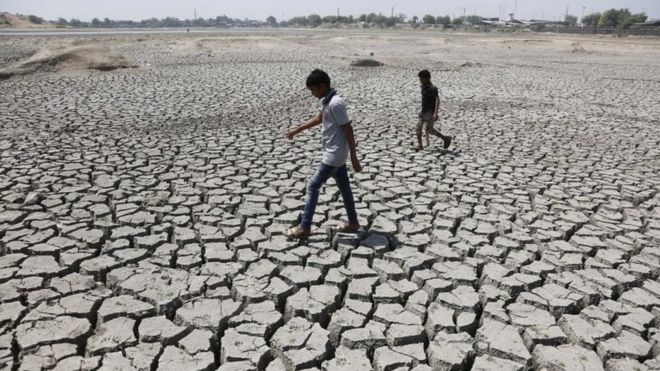 Indian boys on their way to play cricket walk through a dried patch of Chandola Lake in Ahmadabad, India, Saturday, May 14, 2016. M