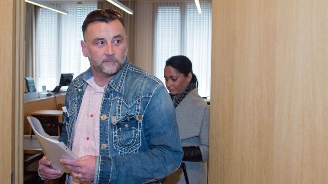 Lutz Bachmann, holding papers, walking through a modern wooden door with a woman behind him