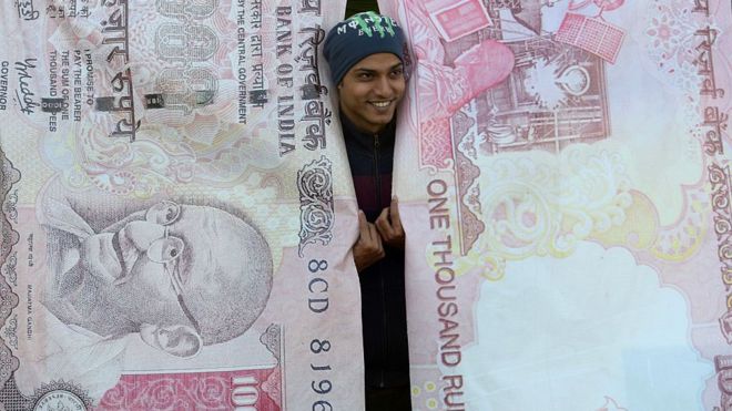 Hombre posando con réplicas de los billetes que cancelaron en India.