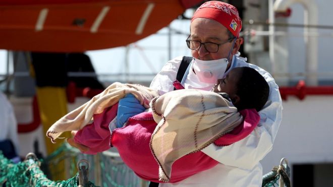 A doctor carries a child as migrants disembark from the MSF vessel at Pozzallo"s harbour in Sicily, Italy, 25 April 2016