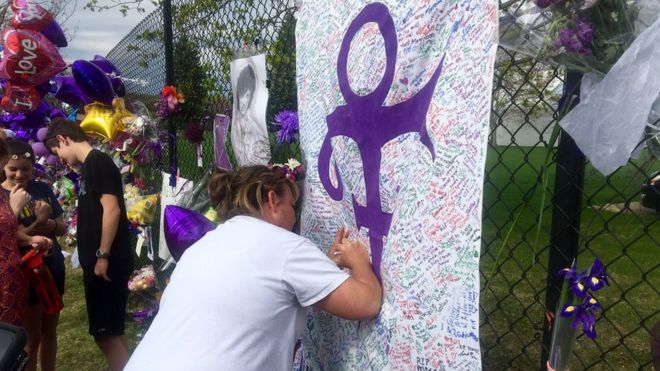 Woman writes on memorial sheet adorned with the symbol Prince once used to identify himself outside Paisley Park