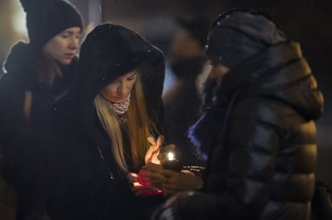 Women try to light a candle to place with flowers in front of the Alexandrov Ensemble building in Moscow, Russia, Monday, 26 December