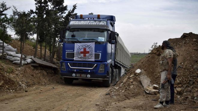 An aid truck of the International Committee of the Red Cross (ICRC) drives past rebel fighters as it enters the rebel-held village of Teir Maalah, on the northern outskirts of Homs in central Syria, on April 25, 2016.