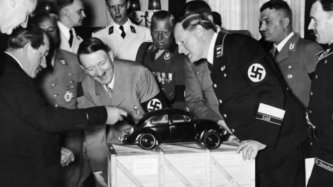 Adolf Hitler looks at a model of the Volkswagen car. He is with the designer Ferdinand Porsche (left),
