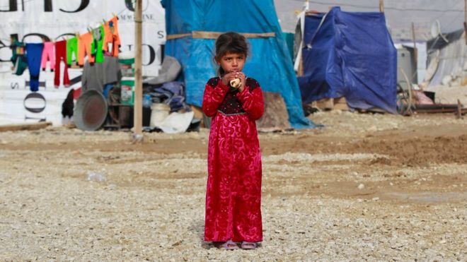 A Syrian girl eats a sandwich as she stands outside her family tent, during the visit of Filippo Grandi, the United Nations High Commissioner for Refugees, UNHCR, to a Syrian refugee camp in the town of Saadnayel, in the Bekaa valley, east Lebanon, Friday, Jan. 22, 2016.