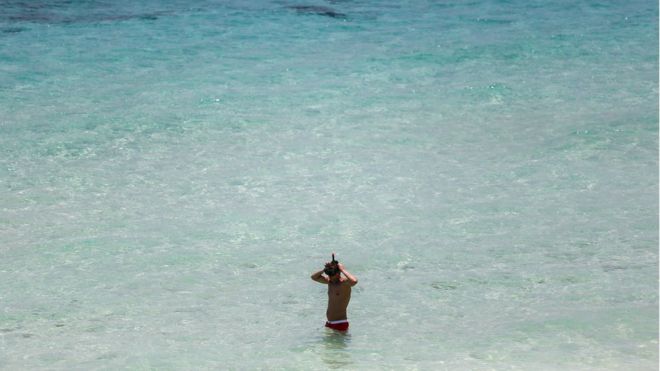 Man wearing a snorkel, standing in the sea on a beach in Phuket