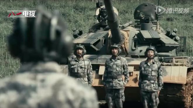 Three men in uniform standing in front of a tank, with the back of the head and shoulders of the man giving them orders in the foreground