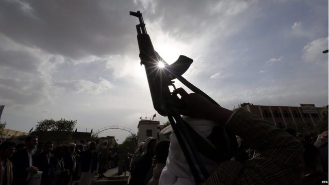 An armed Houthi supporter holds up guns during a protest