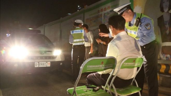 Shenzhen Traffic Police photo showing a man on a chair in the beam of car headlights with a police officer next to him