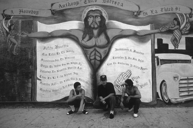 ثلاثة رجال يجلسون أمام رسم جداري يجسد المسيح في لوس أنجليس.
