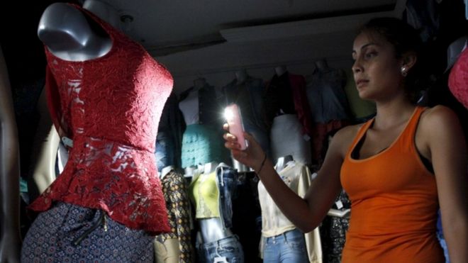 A customer uses her phone's light to look at a dress at a store during a power cut in San Cristobal, in the state of Tachira, Venezuela, April 25, 2016