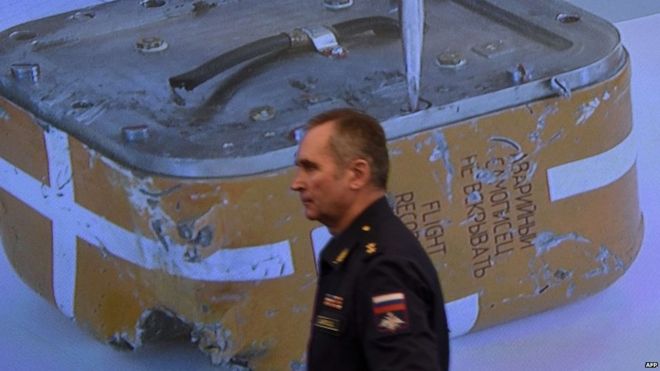 A Russian military official passes by a screen showing a live broadcast of the opening of the flight recorder from the Russian Su-24 bomber in Moscow, 18 December