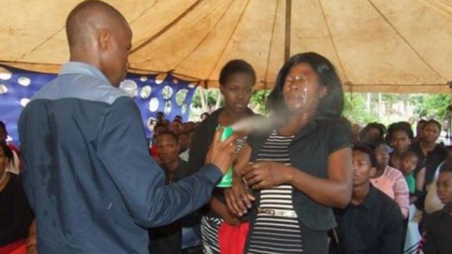 A man spraying insecticide in the face of a woman before a congregation