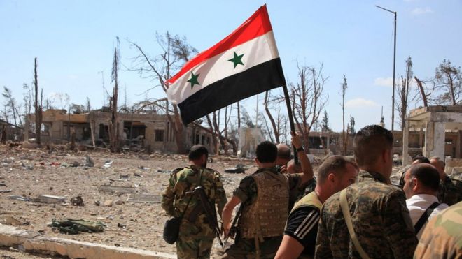 Fuerzas leales al presidente sirio Bashar al-Asad sostienen una bandera siria mientras caminan por un complejo militar recapturado en Alepo (5 de septiembre de 2016).