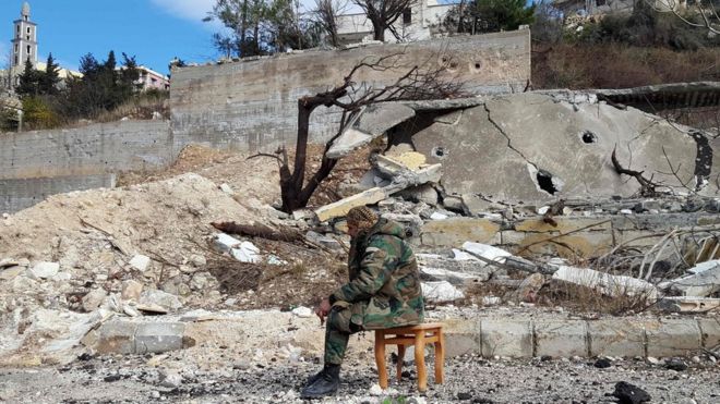 A pro-government soldier sits in a town damaged during Syria's war