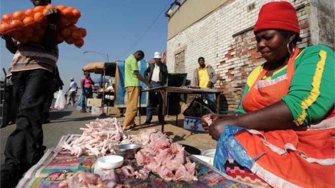 A man carrying oranges walks past a roadside vendor selling chicken strapes at the Alexandra township, near Johannesburg in South Africa.