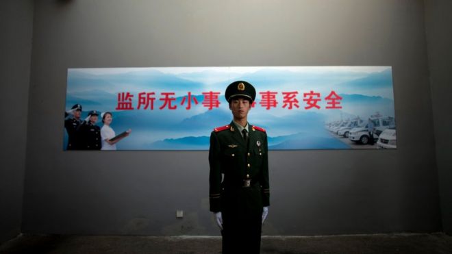 A Chinese paramilitary policeman stands guard underneath a surveillance camera at an entrance to the Number Two Detention Centre in Beijing