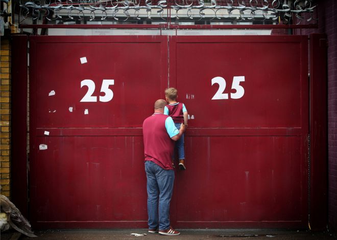 Папа с маленьким сыном наблюдают в щелку ворот за последним матчем клуба "Вест Хэм"