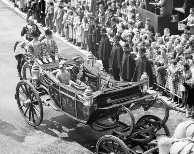 Người dân và cảnh sát đứng dưới trời mưa chào đón Quốc vương Bhumibol của Thái Lan và Nữ hoàng Anh khi họ đi từ Victoria tới Cung điện Buckingham ở đầu chuyến thăm Anh Quốc năm 1960