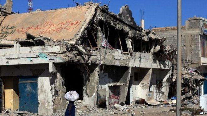 A Libyan woman walks past the rubble of a building in the Mediterranean city of Sirte on 13 October 2012