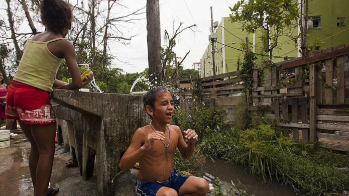 Criança toma banho ao lado de um esgoto na Cidade de Deus, no Rio de Janeiro