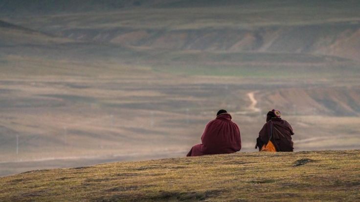 Dos tibetanos sentados en un paisaje montañoso, de espaldas