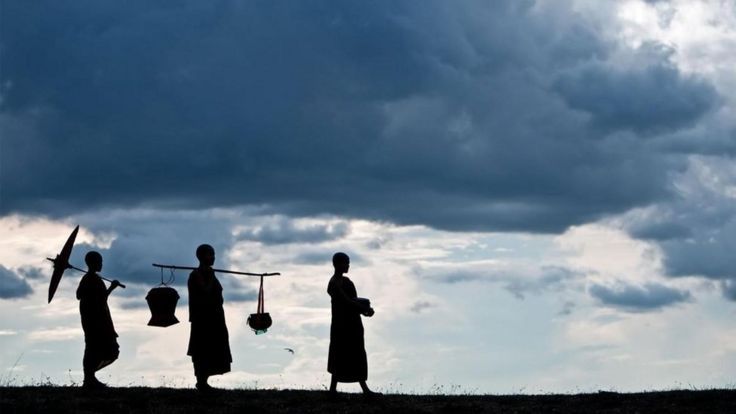 Tres tibetanos caminando contra un fondo de nubes, en contraluz