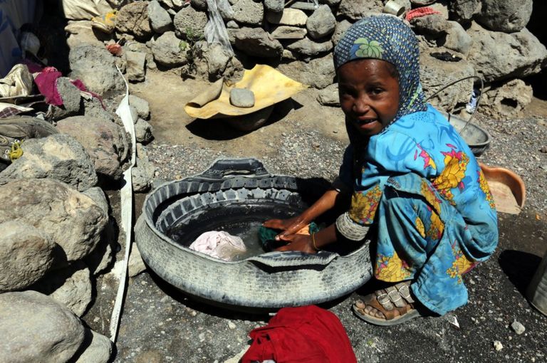 A small girl washes clothing in a makeshift container